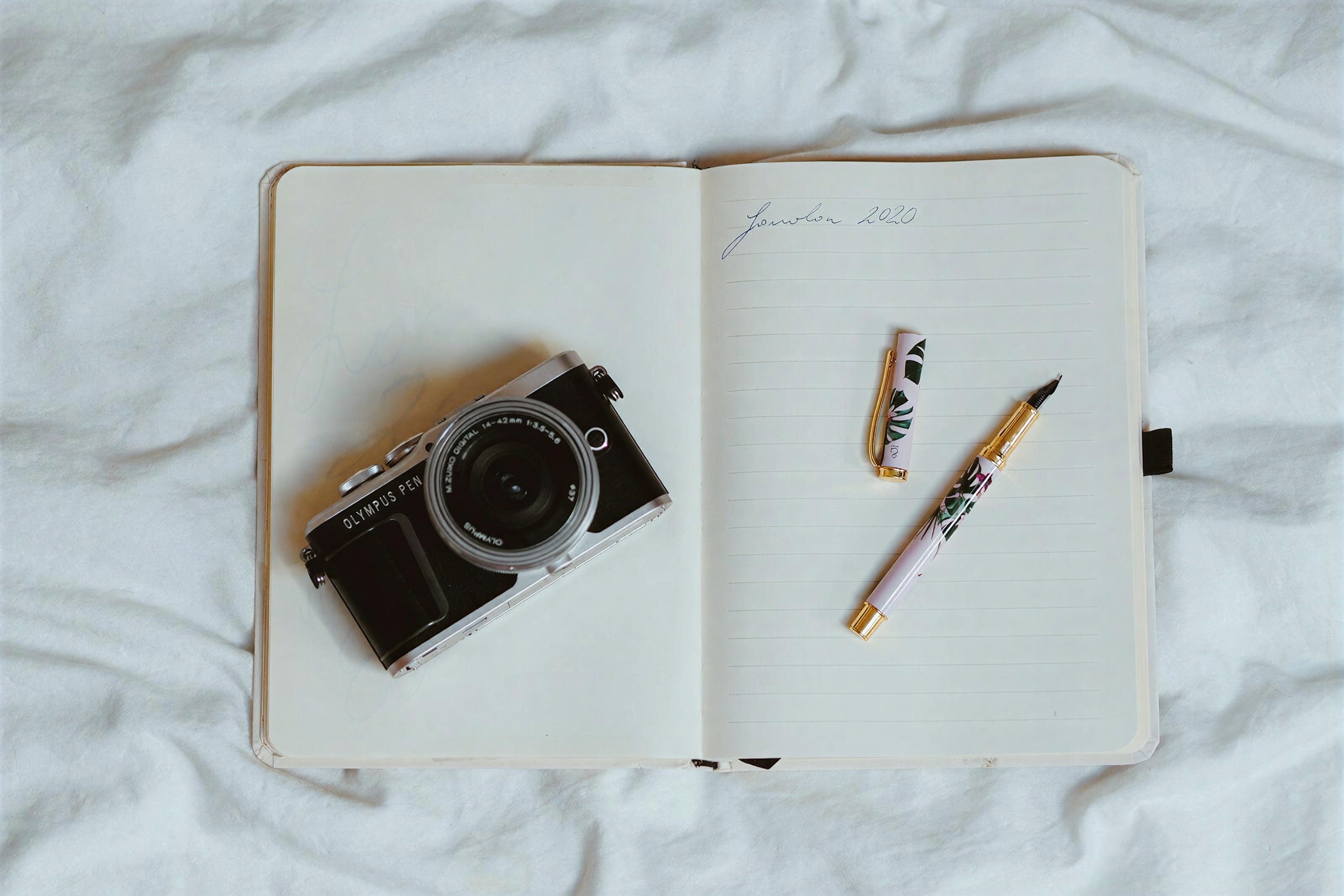 An open notebook, a film camera and a pen on white linen