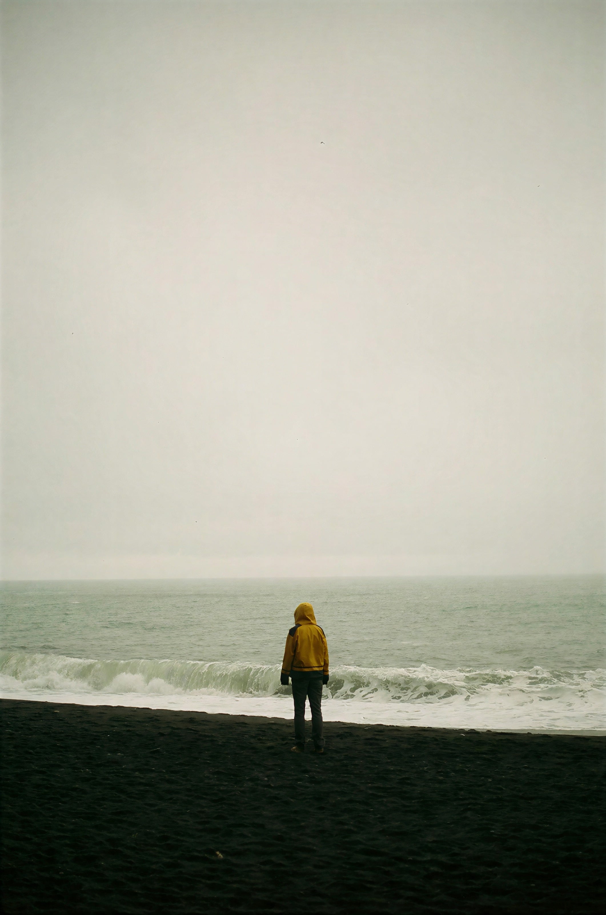 A walker in a yellow coat on an empty beach in morning haze