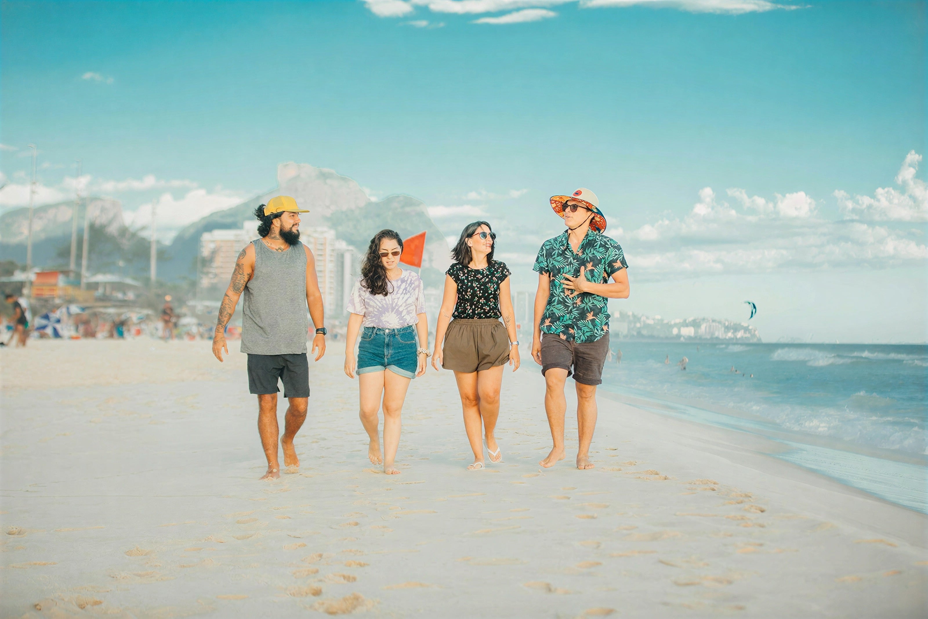 Four friends walking barefoot along a sandy beach