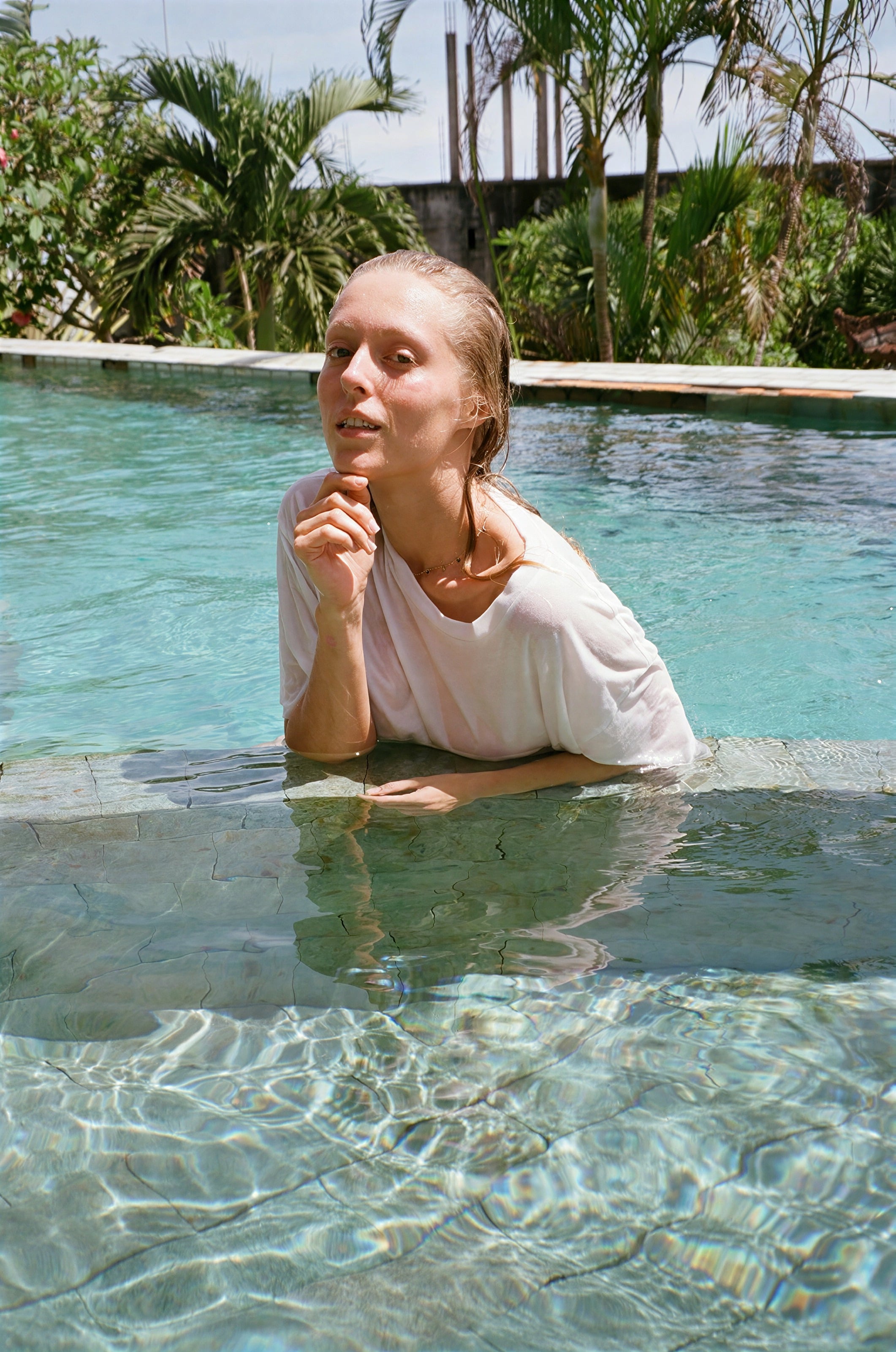 A woman resting at the edge of a pool among palms