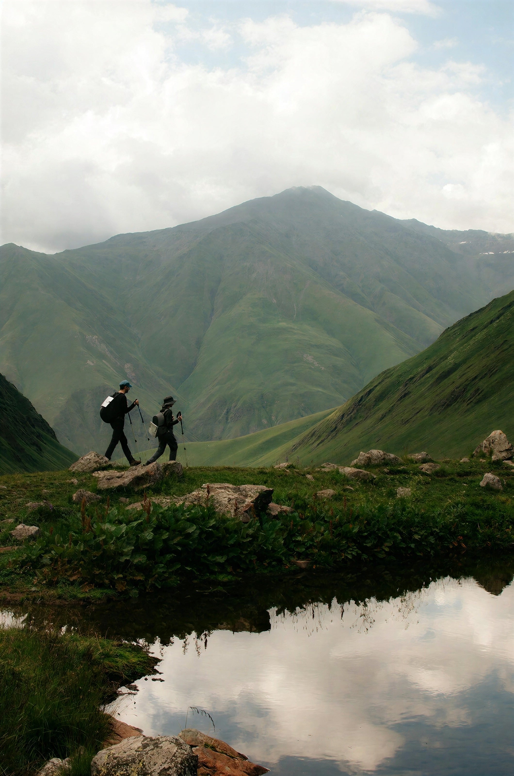 Two walkers on a ridge above an alpine lake