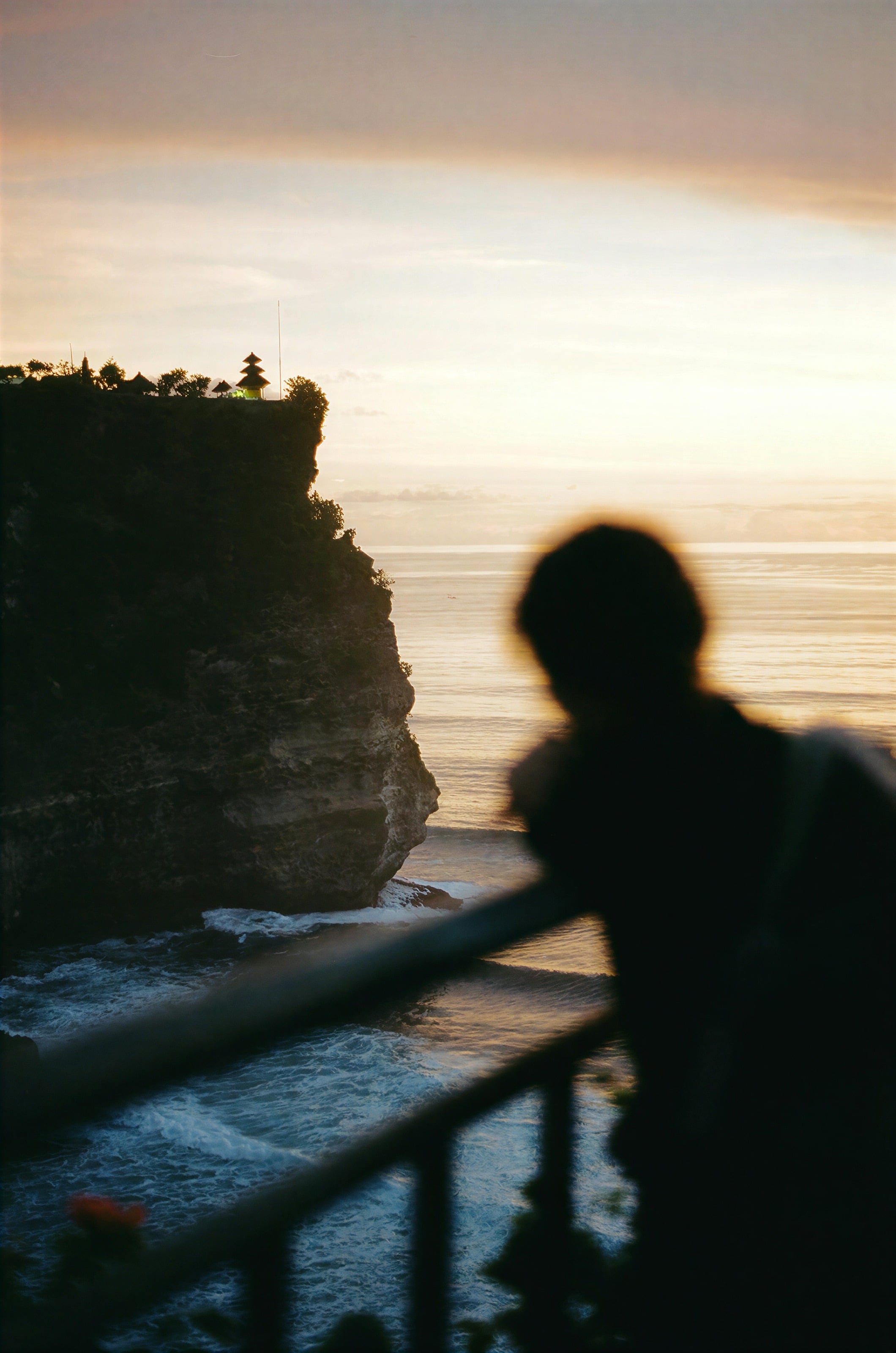 A silhouette at a railing above sea cliffs at sunset in Bali
