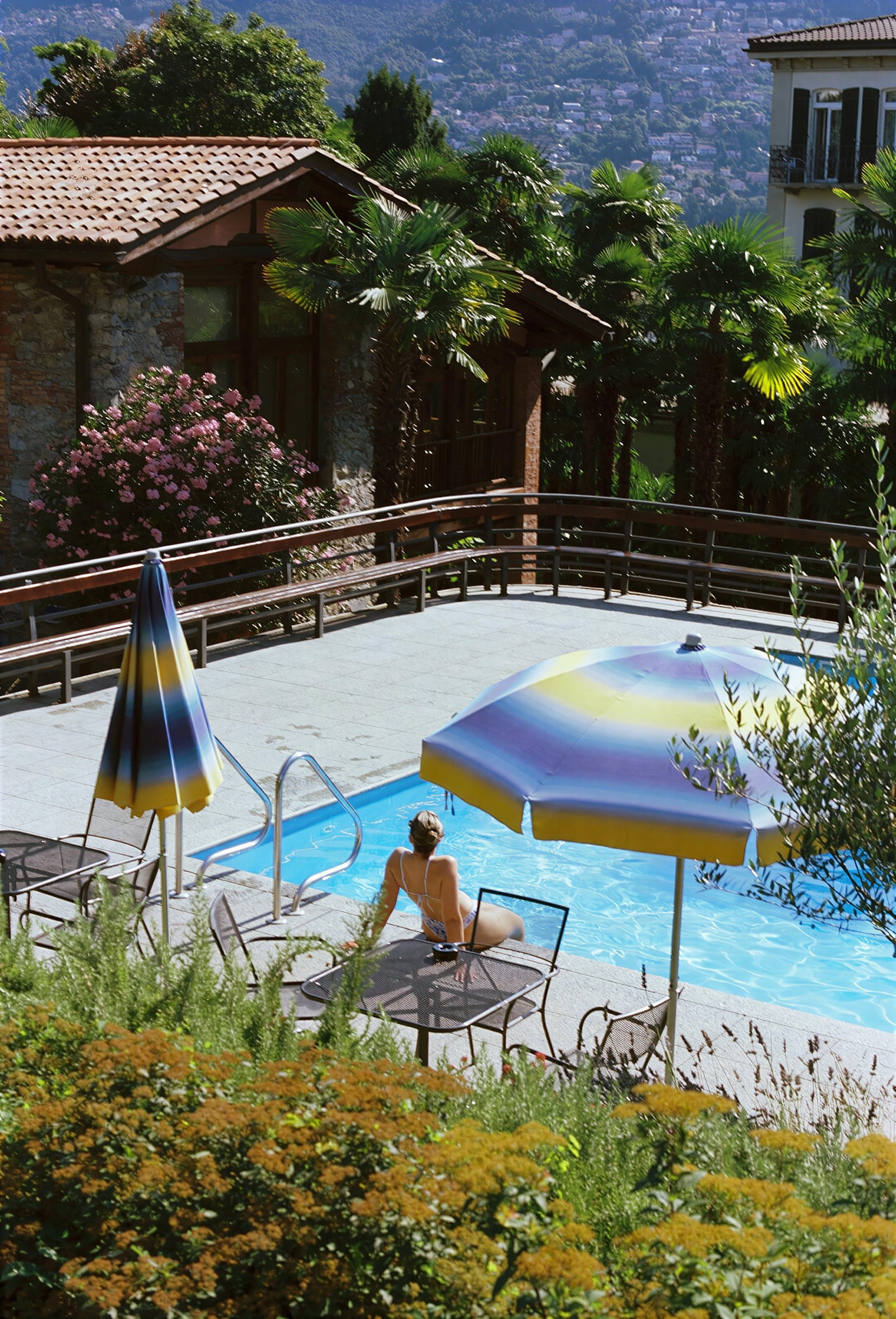 A guest reading by a garden pool under striped umbrellas