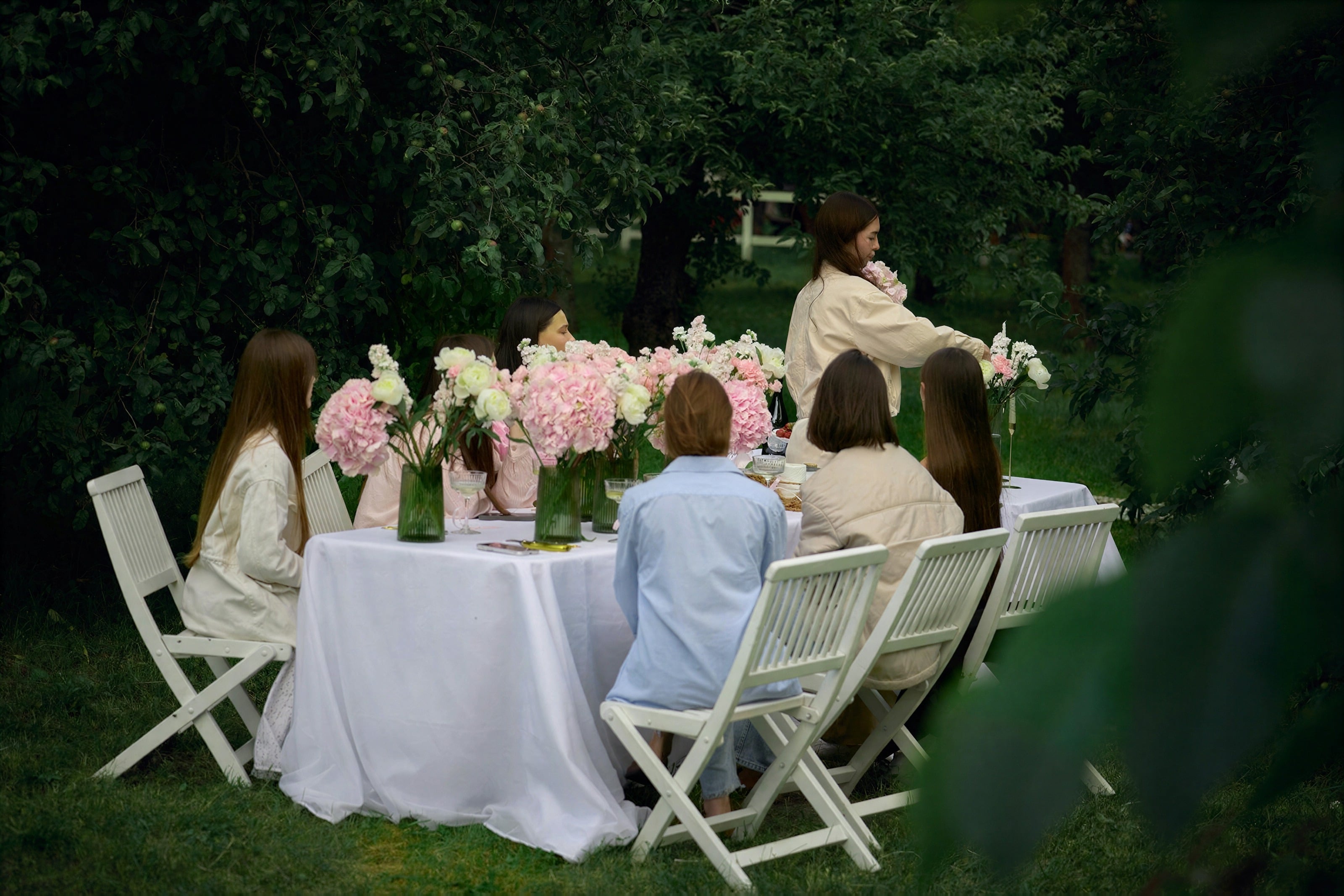 A group sharing a long table set with flowers in a garden
