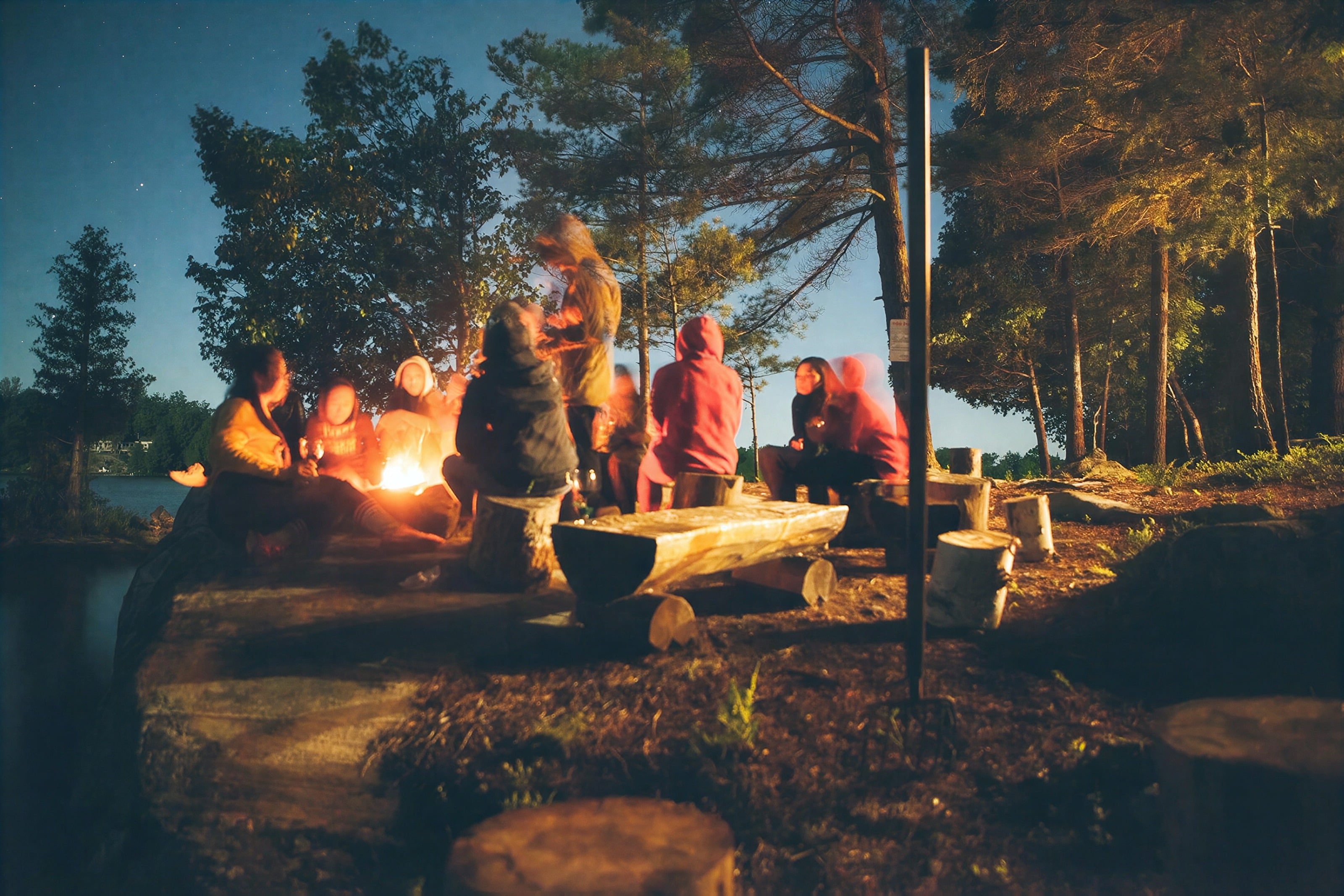 Un grupo reunido alrededor de una hoguera junto a un lago al atardecer